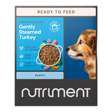 A package of Nutriment dog food featuring a puppy and a bowl of gently steamed turkey and beef dog food. The package is marked as 'ready to feed' and has a grain-free label, with a visual of a dog on the front.